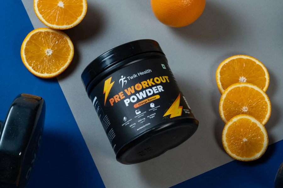 Black container of Twik Health Pre-Workout Powder surrounded by orange slices and a dumbbell on a blue and gray background.